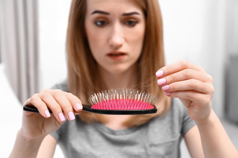 Woman pulling hair out of hairbrush because of seasonal spring shedding